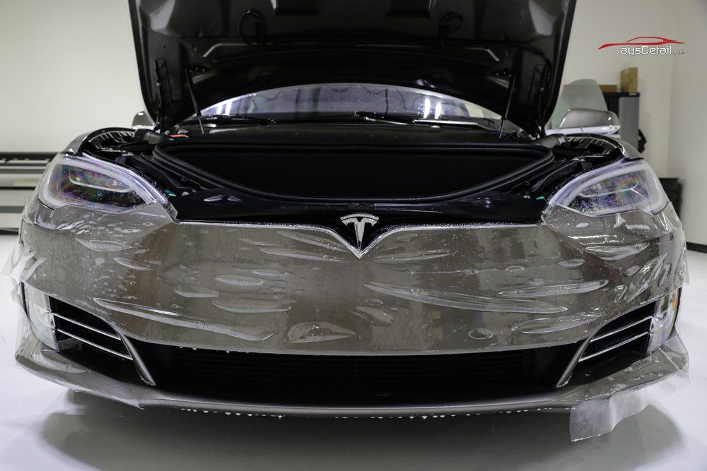 Tesla Model S with clear protective film on the front, hood open, indoor setting.