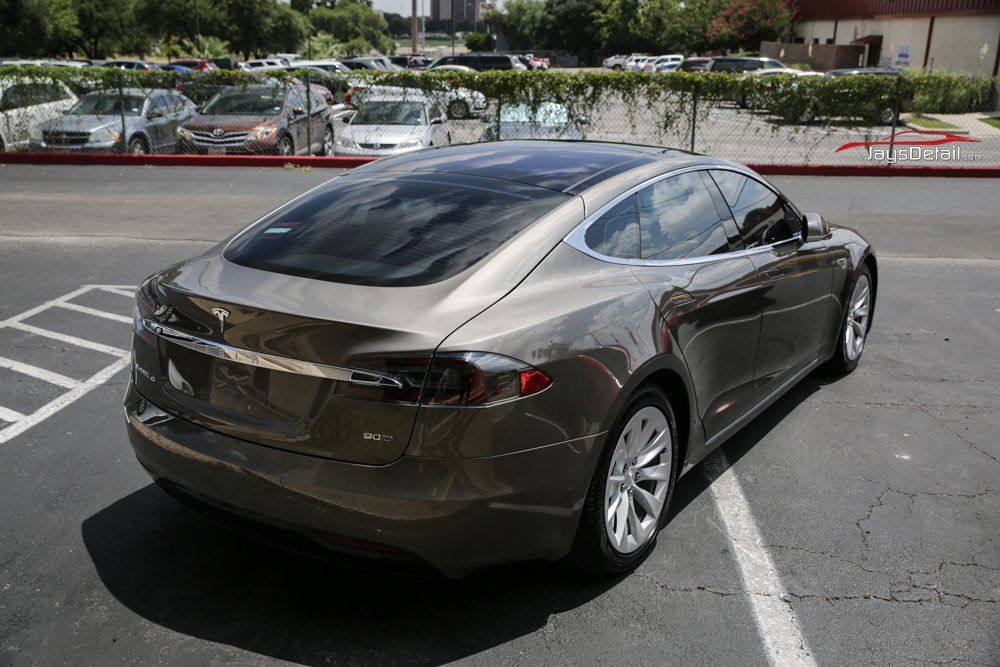 A brown Tesla sedan parked in a lot on a sunny day.