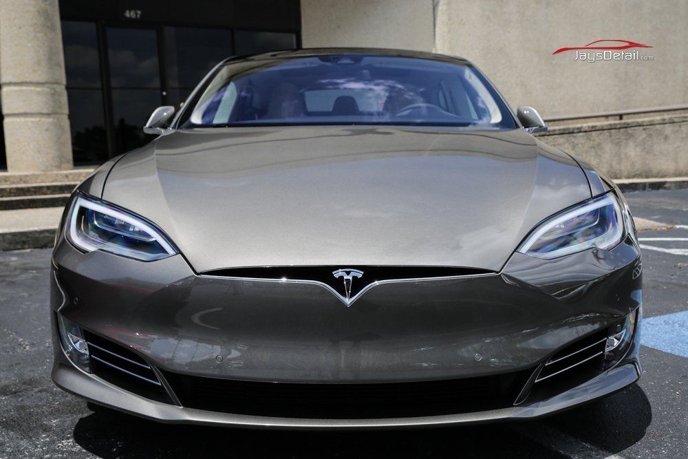 Gray Tesla Model S parked in front of a building with bright headlights.