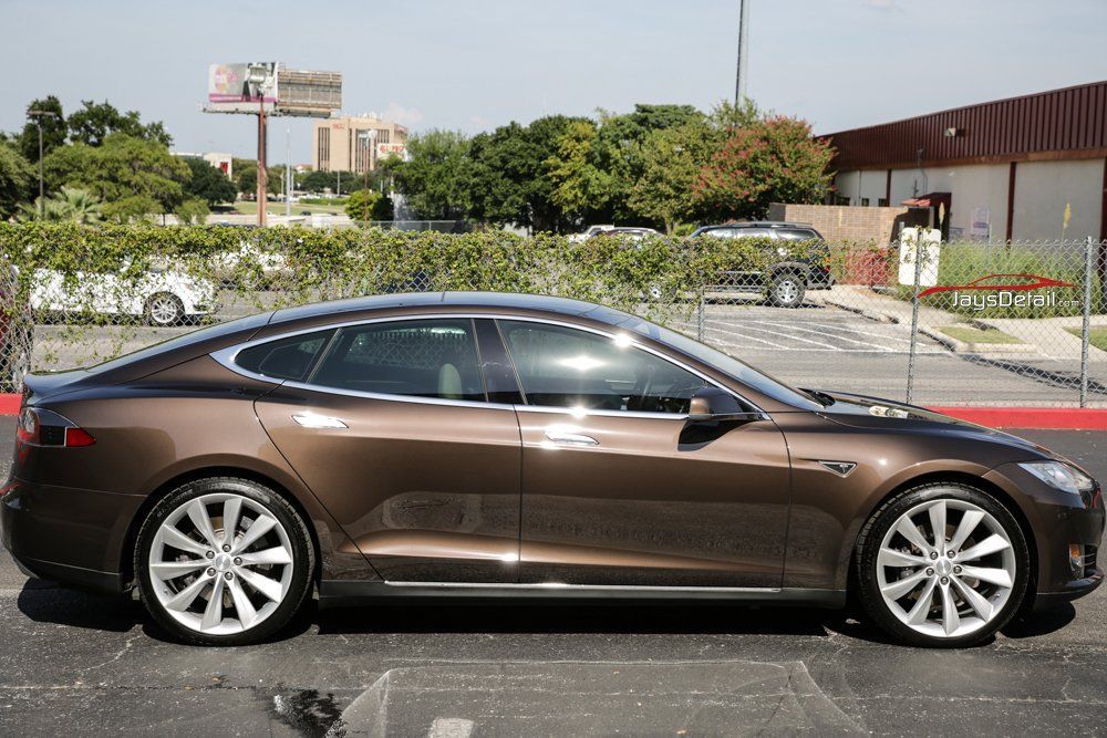 Brown Tesla Model S parked in front of a building, showcasing its sleek design and wheels.