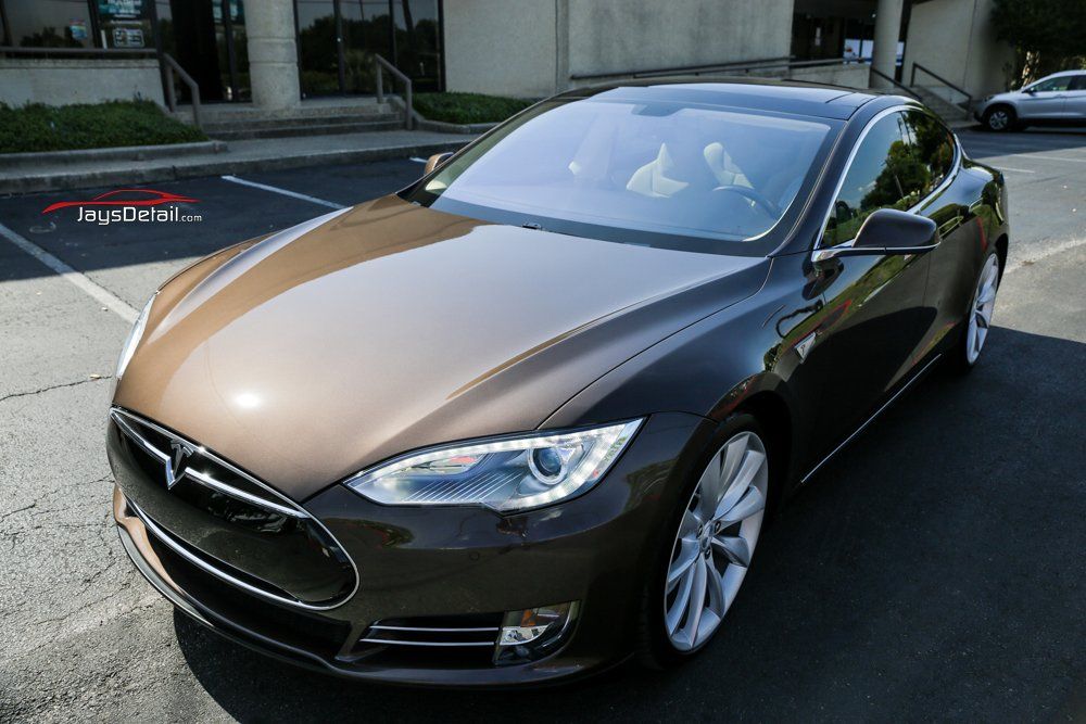Brown Tesla sedan parked in a parking lot on a sunny day.