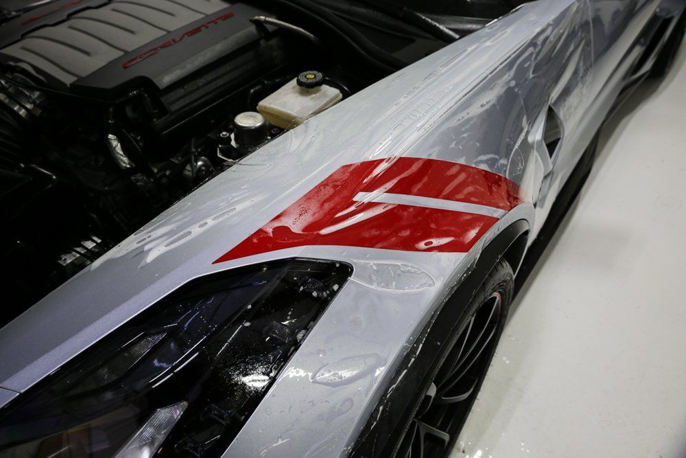 Silver sports car fender with red and white racing stripe, hood open.