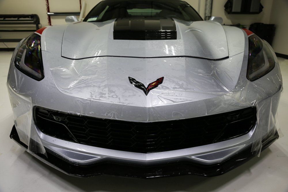 Silver Corvette sports car with protective film on the front, indoors.