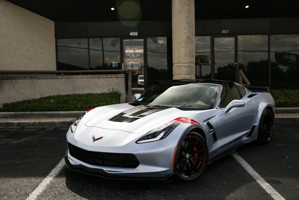 Silver Corvette sports car parked in front of a building with black windows.