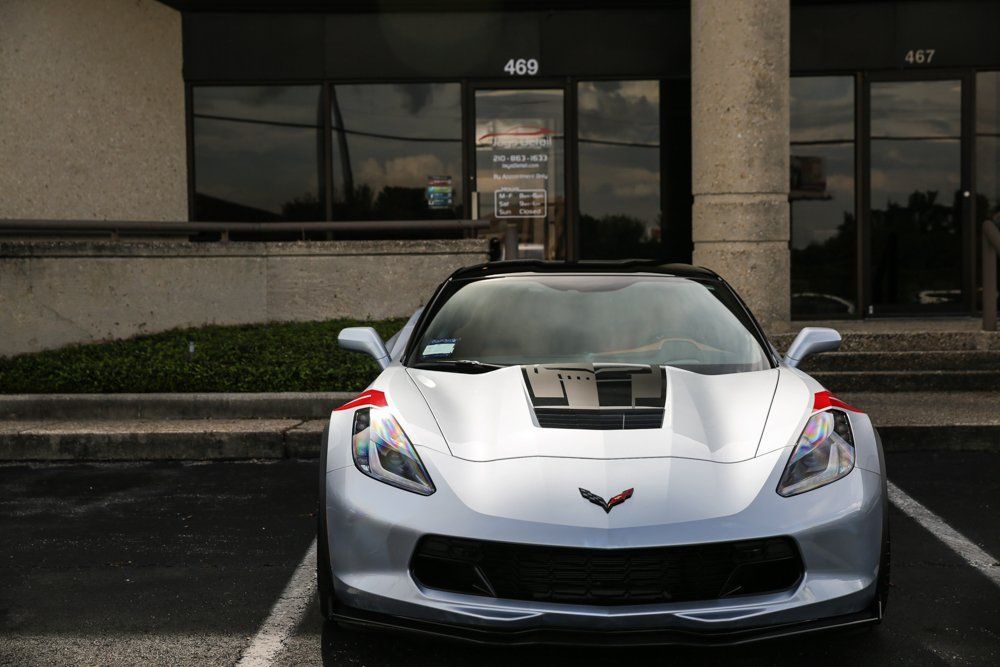 Silver Corvette sports car parked in front of a building with glass doors, exterior shot.