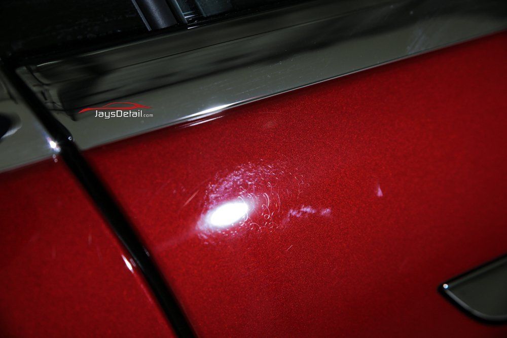 Red car door with scratches, highlighting damage with a bright light.