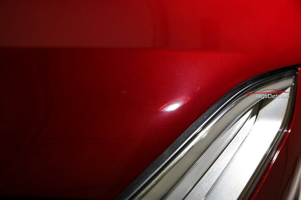 Red car hood with a dent and chrome trim.