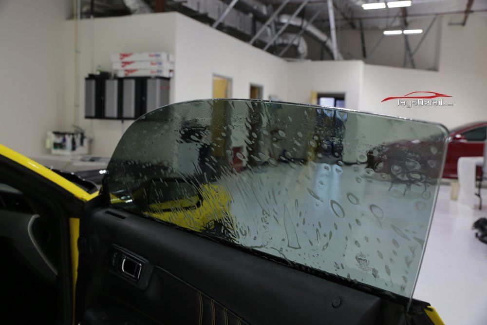 A yellow car door with tinted window being installed in a garage.