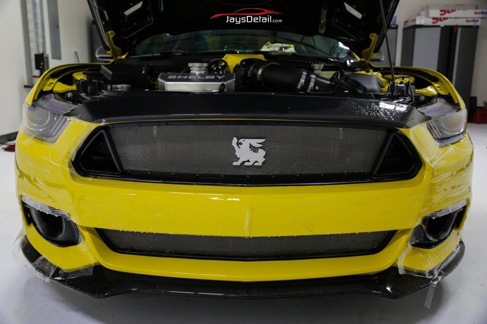 Yellow Ford Mustang with black accents, open hood, and custom grill, indoors.