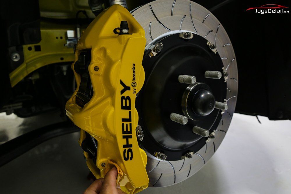 Yellow Shelby brake caliper on a car wheel with a silver, slotted rotor.