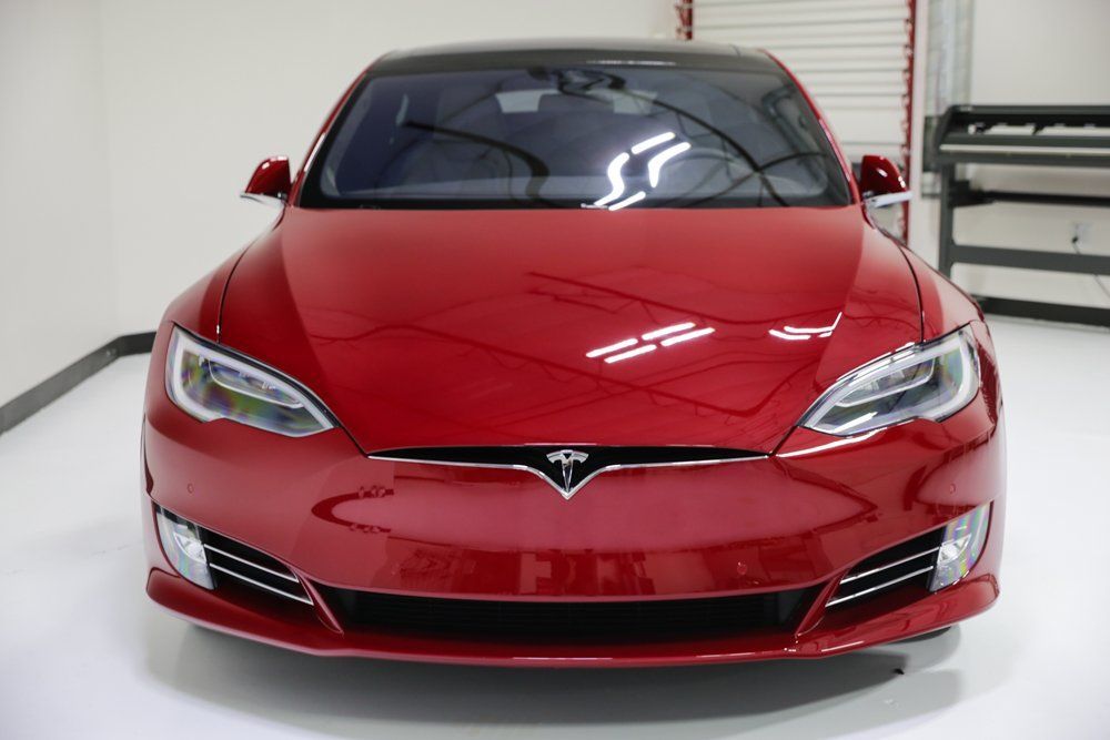 Red Tesla electric car, front view, black roof, parked indoors.