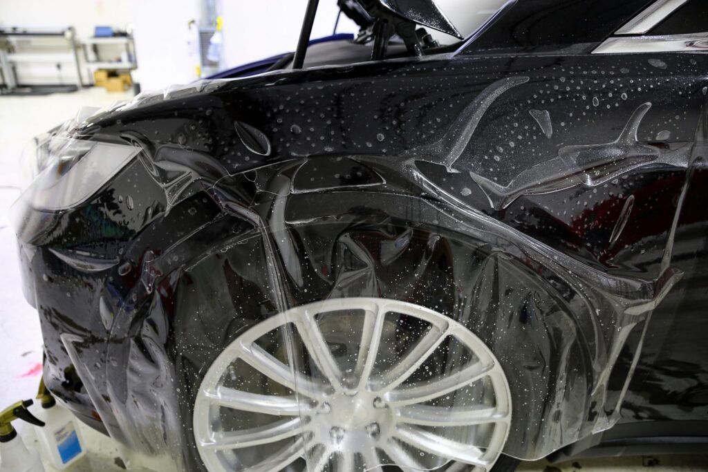 Car's front fender wrapped in clear protective film, with a silver wheel visible.