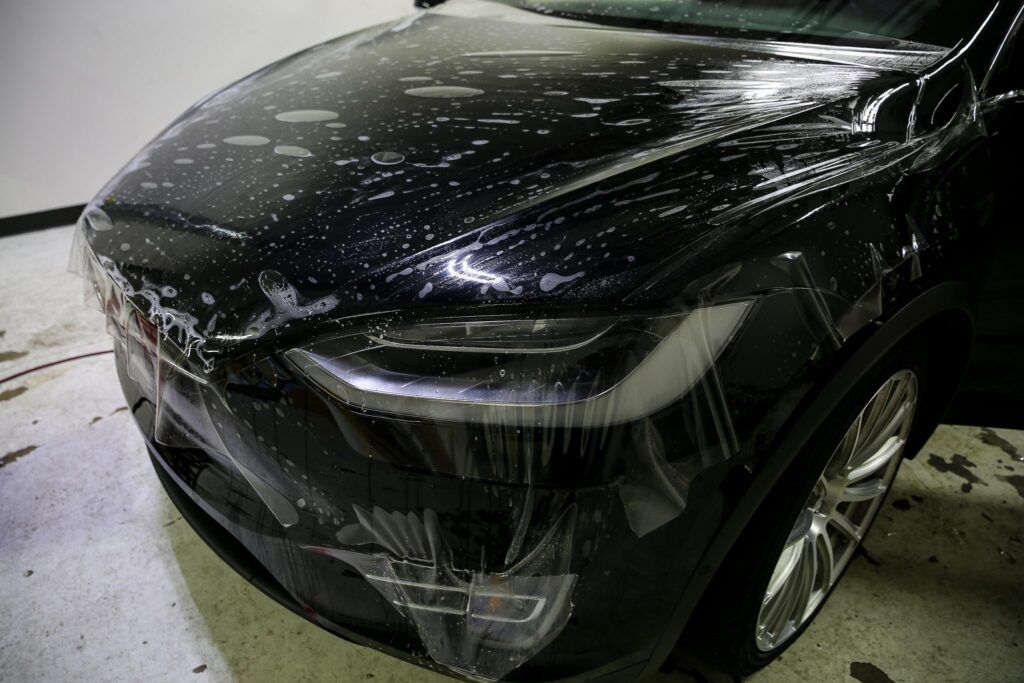 Black car hood with clear film applied; shop setting.