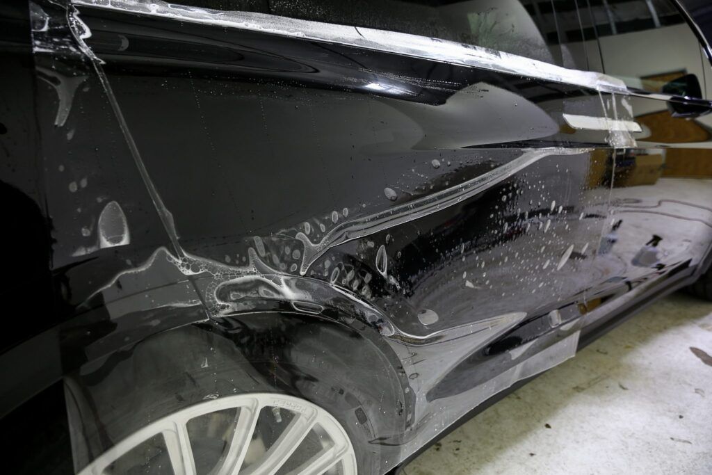 Black car being wrapped in protective film in a garage.