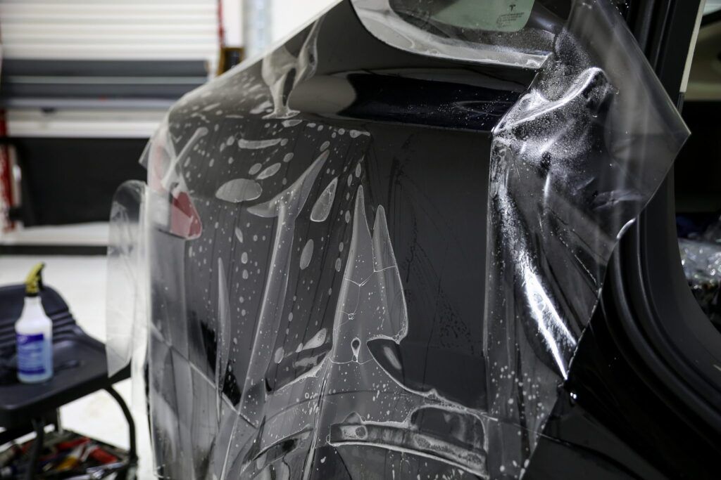 Clear protective film being applied to a black car's rear quarter panel.