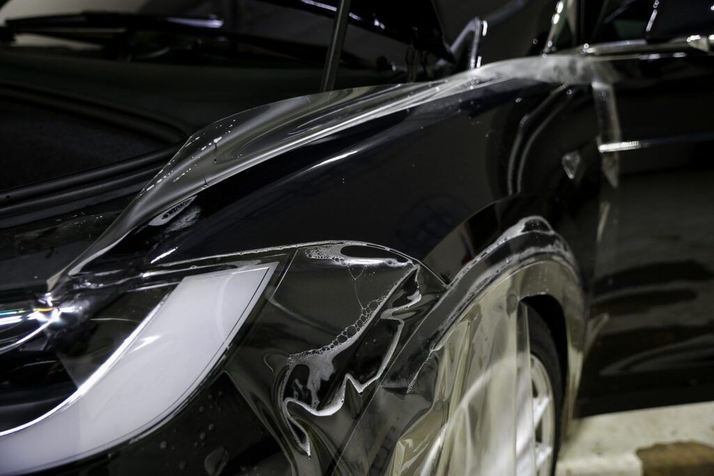 Black car being washed, water cascading over the hood and front fender, glistening with suds.