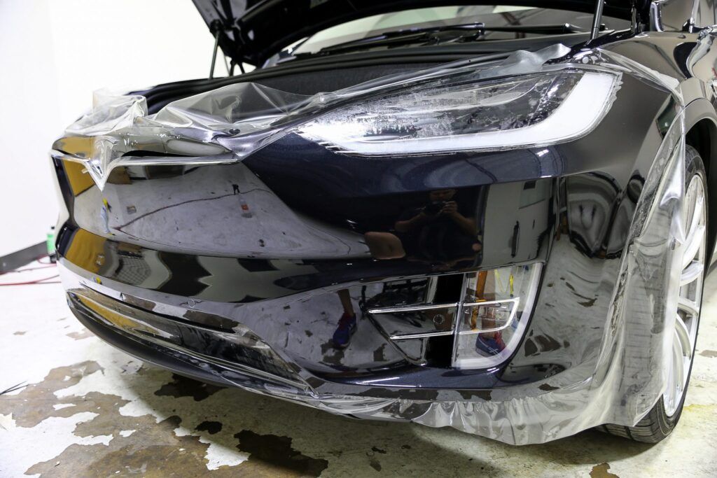 Black Tesla with clear protective film on the front bumper and headlights.