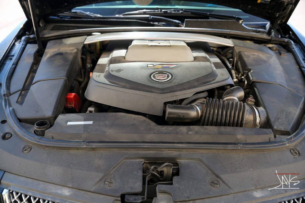 Black car engine bay with engine cover and air intake. Cadillac logo visible.