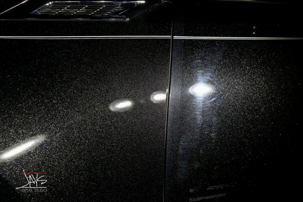 Close-up of a black car door with a textured surface reflecting bright lights.