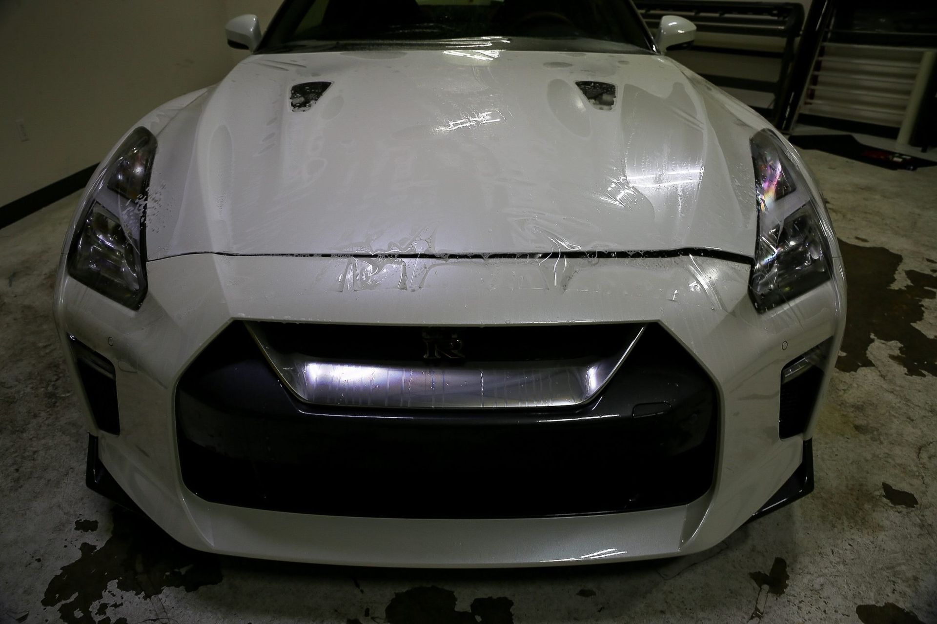 White Nissan GT-R sports car, front view. Features black grill, vents on the hood, and glossy paint in an indoor setting.