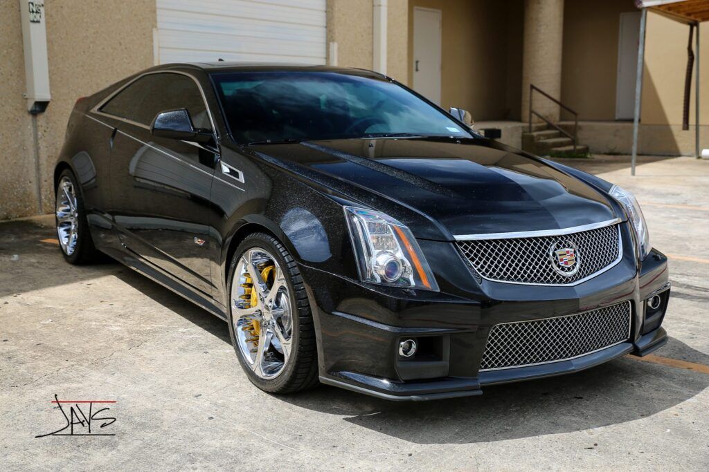 Black Cadillac CTS-V coupe parked in front of a building with tinted windows and custom wheels.