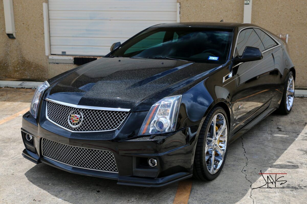 Black Cadillac CTS Coupe with chrome accents parked in front of a building.