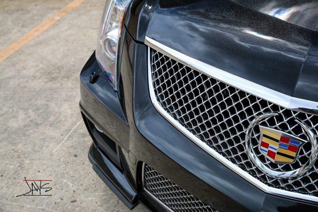 Black Cadillac CTS-V front grill with Cadillac emblem, shiny chrome, on pavement.