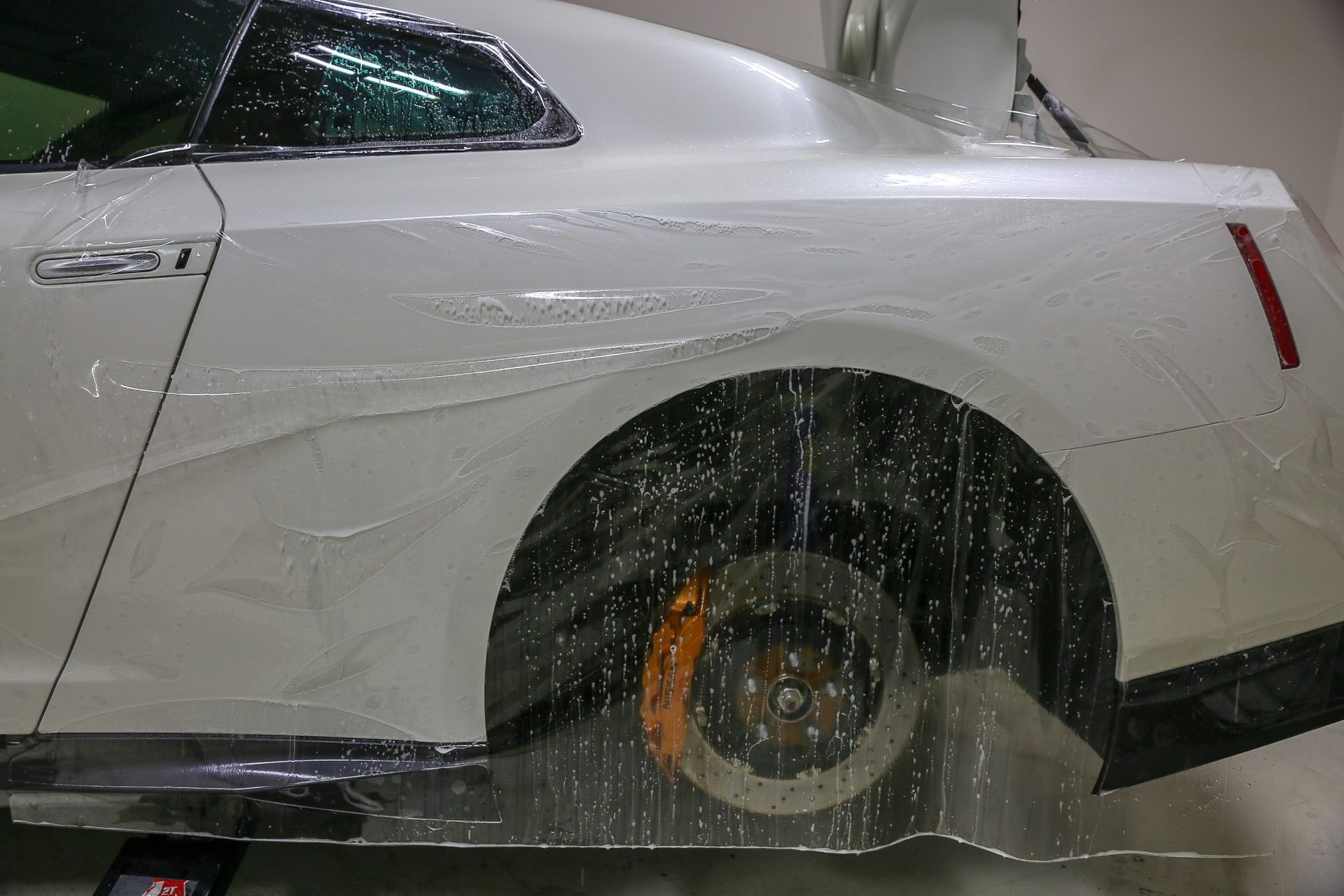 White sports car with protective film over rear quarter panel and wheel.