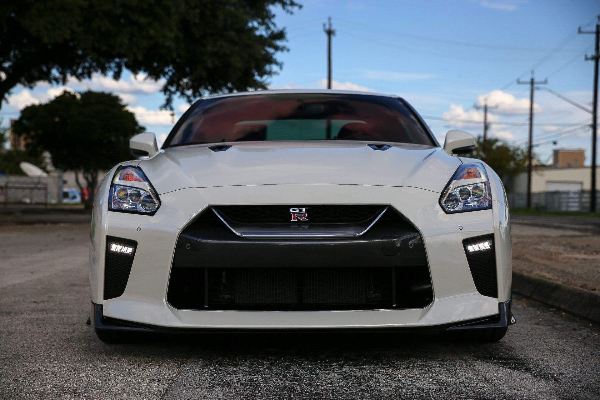 White Nissan GT-R sports car parked on a road, front view, black grill, daytime.