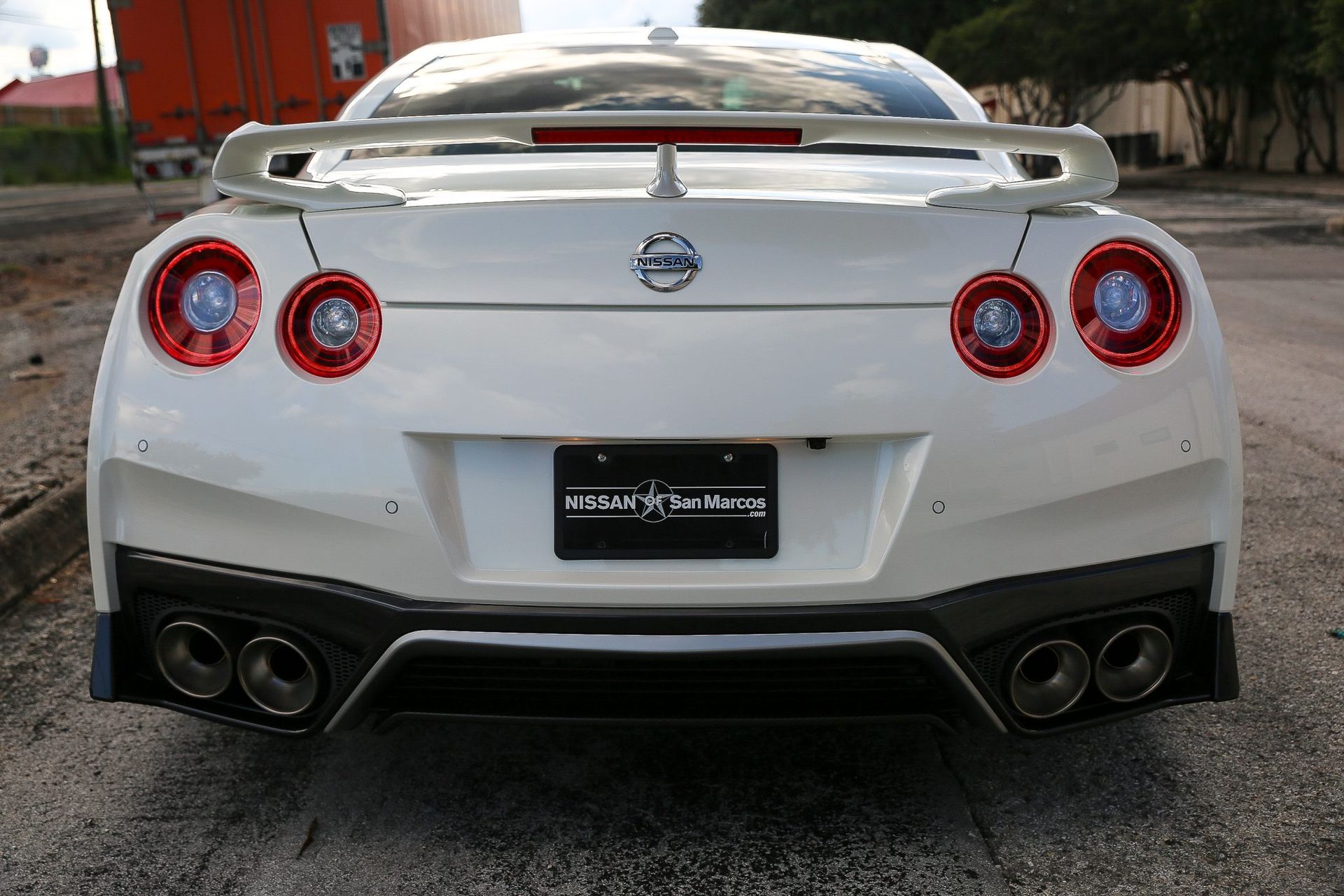White Nissan GT-R sports car rear view, with four exhaust pipes, red taillights, and a spoiler.