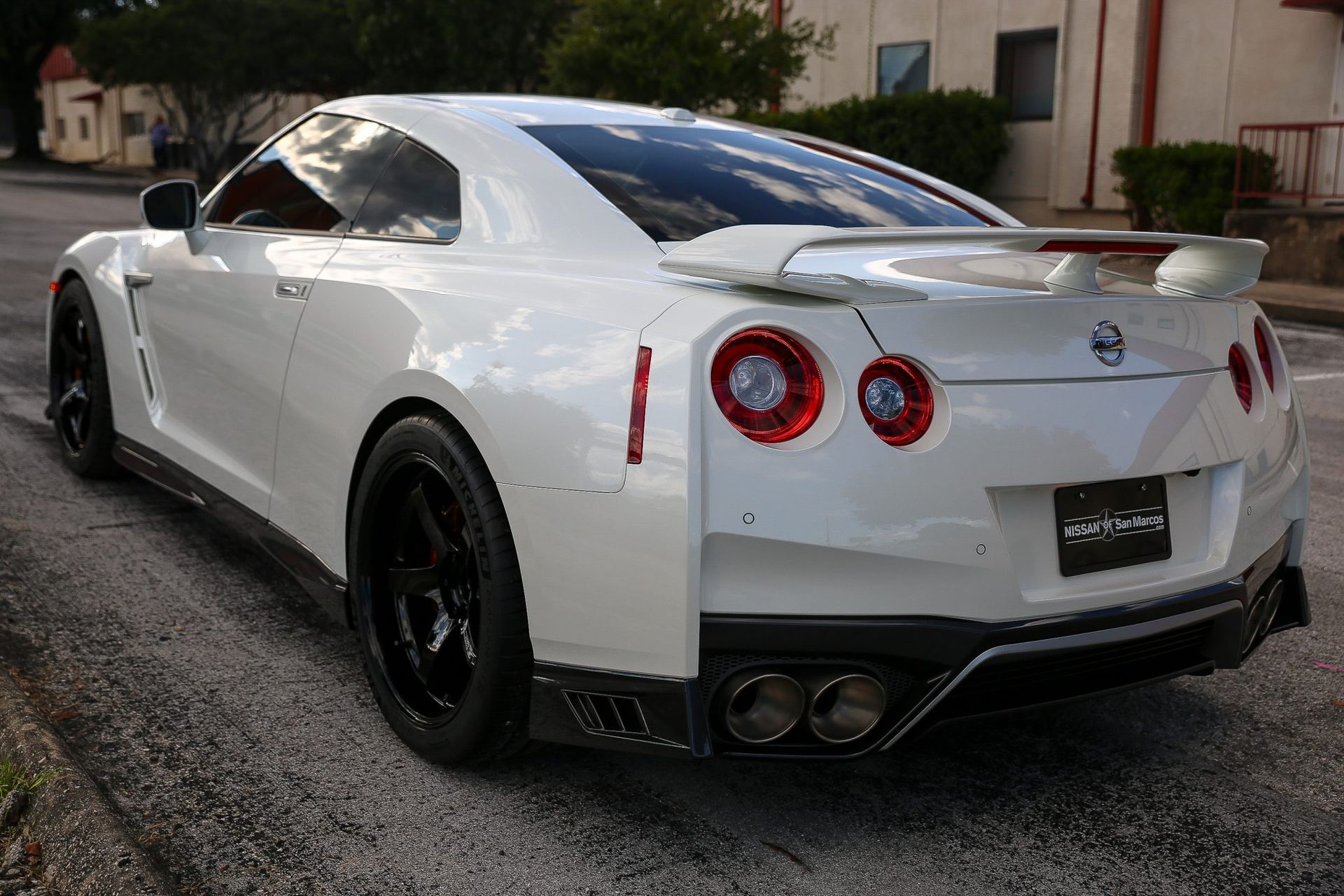 White Nissan GT-R sports car parked on a street, rear view showing black wheels, spoiler, and exhaust.