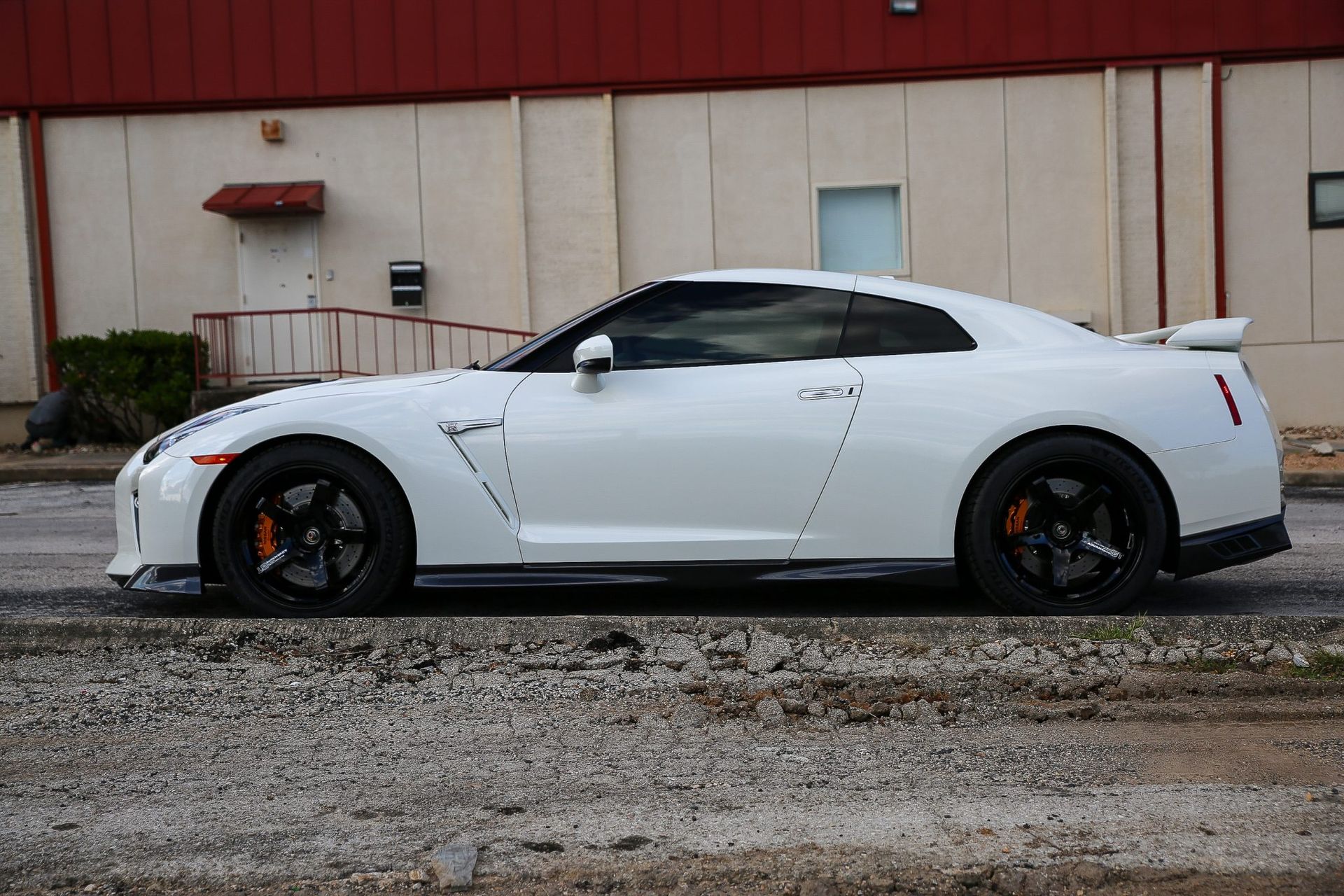 White Nissan GT-R sports car with black wheels and orange brake calipers, parked in front of a building.