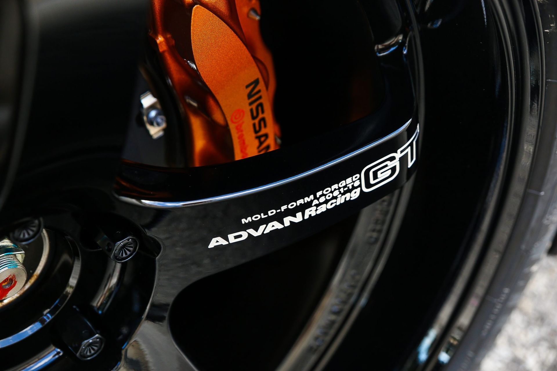 Black car wheel with orange Nissan brake caliper and white 