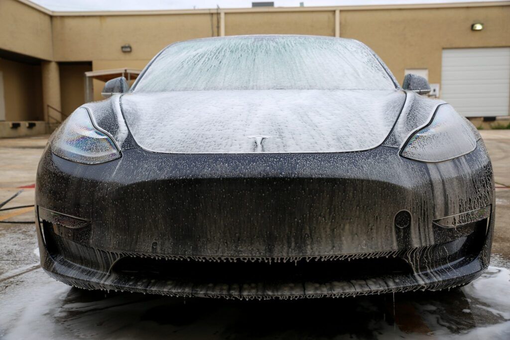 Dark gray Tesla Model 3 covered in white foam at a car wash.