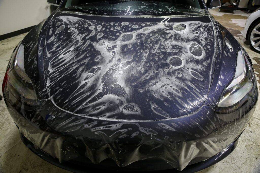Dark blue car hood covered in protective film with bubbles.