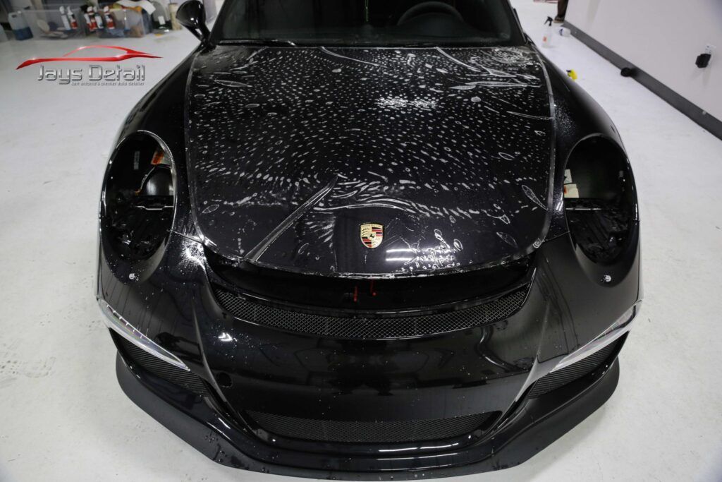 Black Porsche sports car with protective film on its hood in a well-lit shop.
