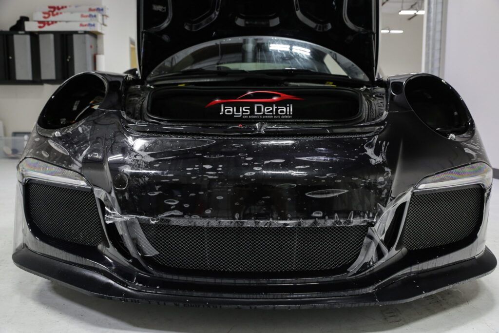 Black Porsche with hood open, in a garage. Carbon fiber details on front bumper.