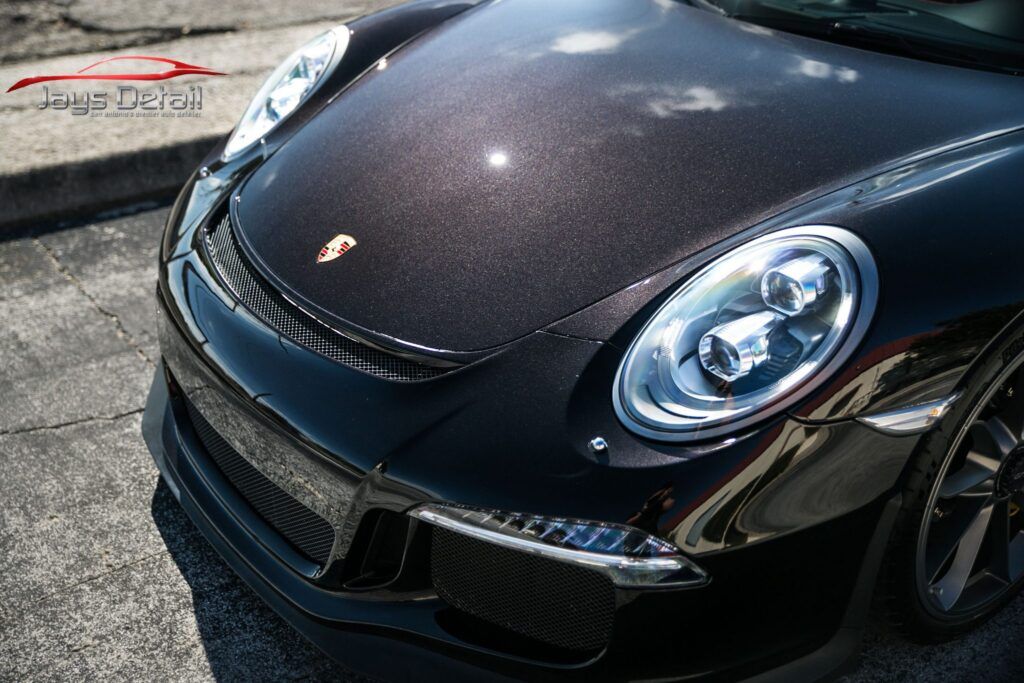 Black Porsche 911 with carbon fiber hood, parked on asphalt, close-up of the front.