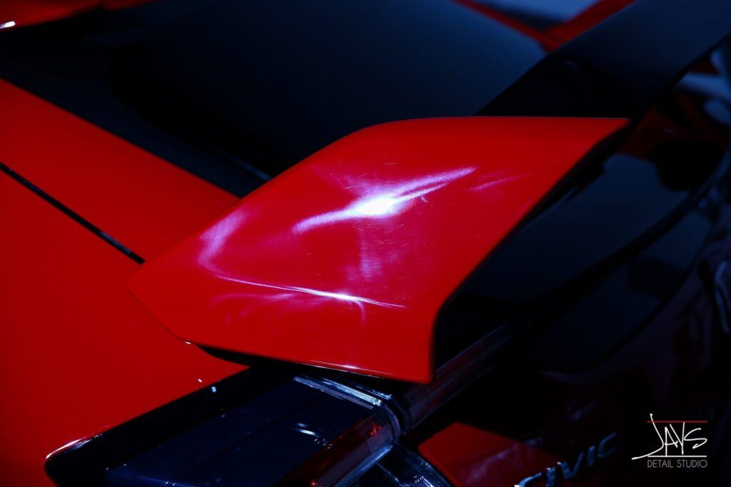 Red car detail with white streaks on the hood, reflecting light against a dark backdrop.