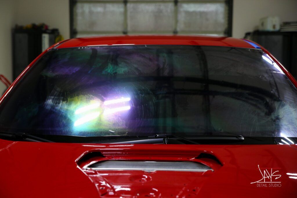 Red car with iridescent tinted windshield, bright garage lights reflecting.