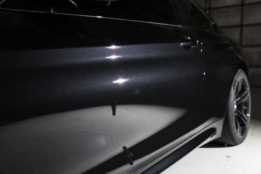Black car door, close-up, reflecting light, showing metallic paint, and a dark tire.