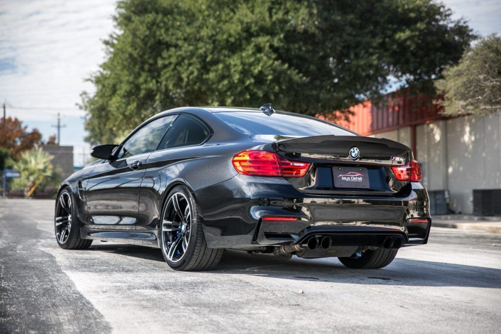 Black BMW M4 coupe parked on a street, showcasing custom wheels and rear spoiler.