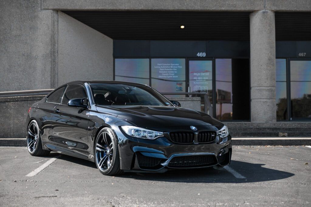 Black BMW M4 coupe parked in front of an office building.