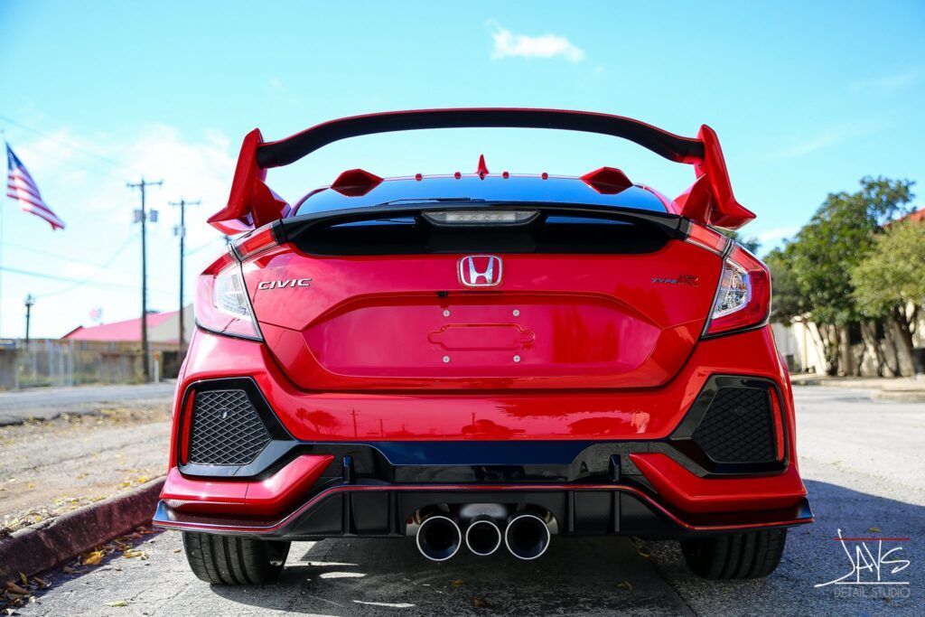 Red Honda Civic Type R from the rear, large spoiler, triple exhaust, and black accents, outdoors.