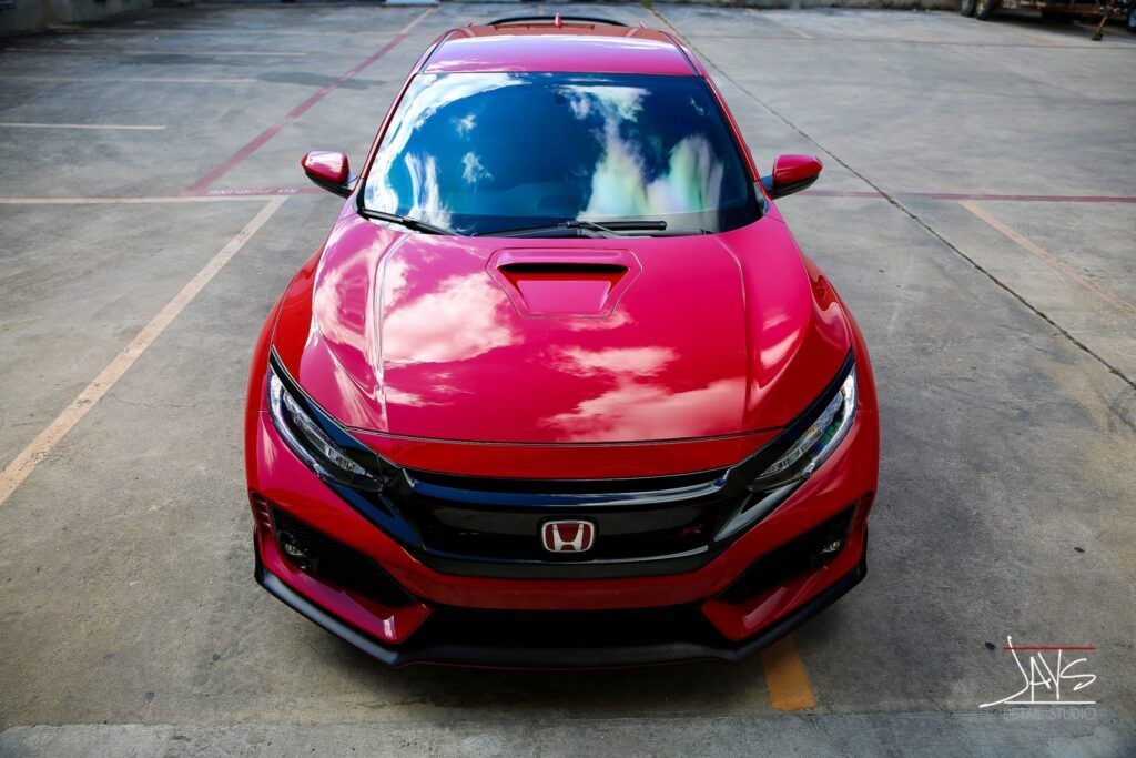Red Honda Civic parked in an empty lot, reflecting the sky in its windshield.