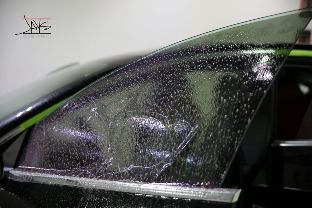 Car window with tinted film applied, showing wrinkles and water drops.