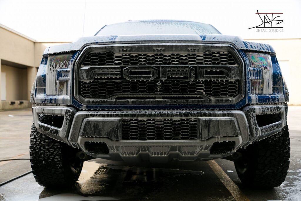 Blue Ford Raptor truck covered in soapy foam during a car wash.
