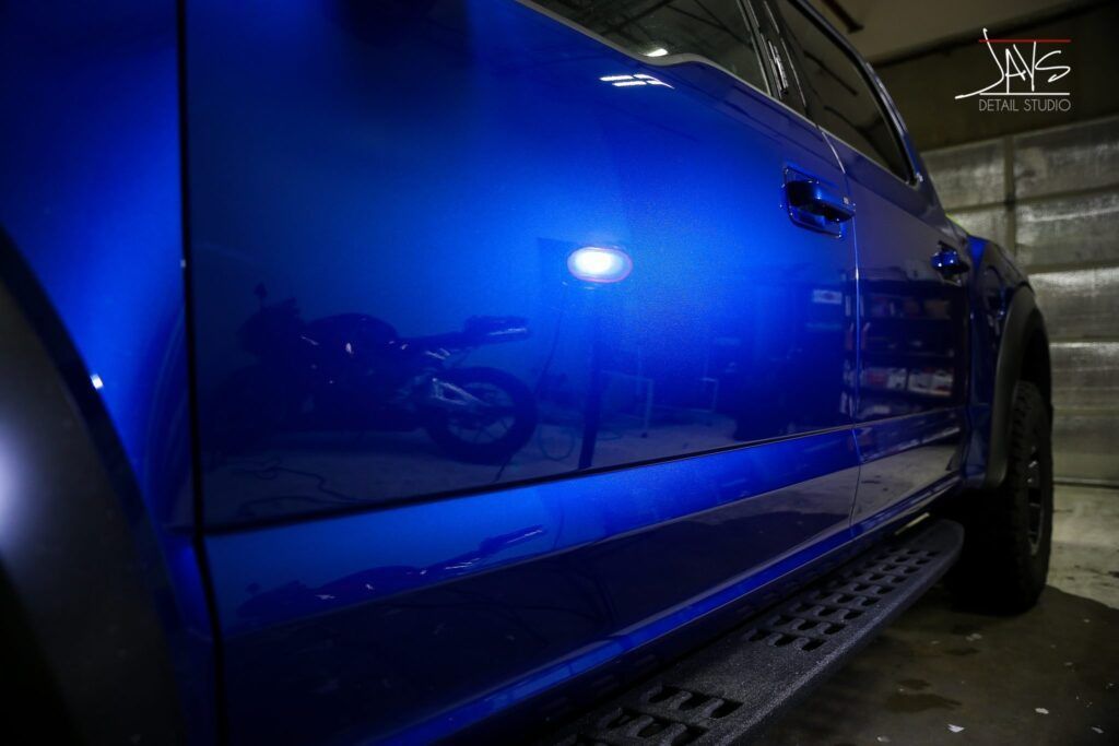 Blue truck door reflecting a motorcycle in a garage setting.