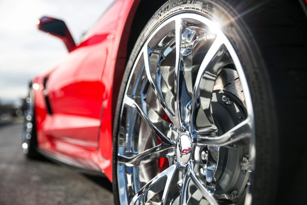 Red sports car, close-up of chrome wheel reflecting sunlight.