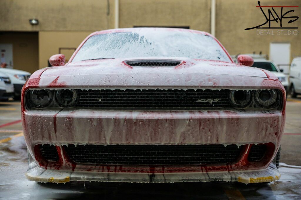 Red Dodge Challenger covered in car wash foam.